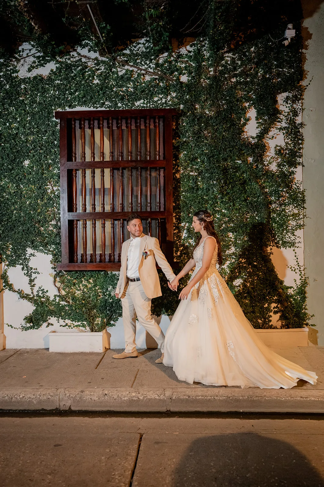 Los novios de la mano frente a una fachada cubierta de enredadera en Cartagena, por Omar Fraija